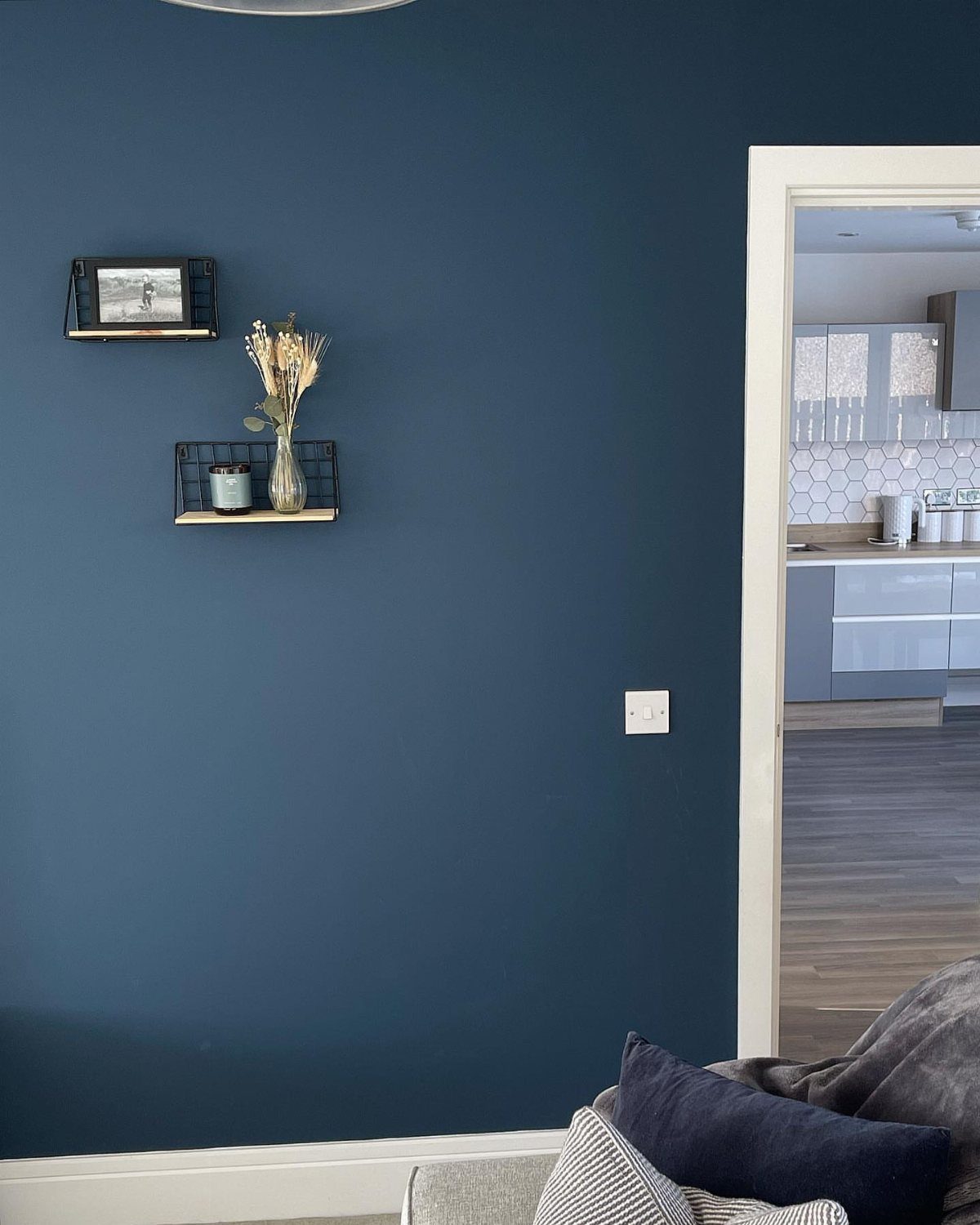 12 Blue White Living Room Ideas with Photos and Styling Tips 5 Deep blue feature wall with small black shelves and a view into a kitchen.