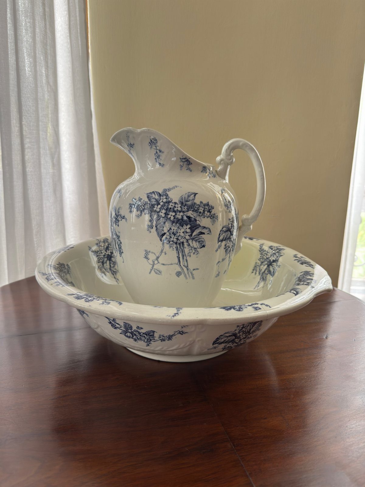Blue and white floral ceramic pitcher and basin on a dark wooden table.